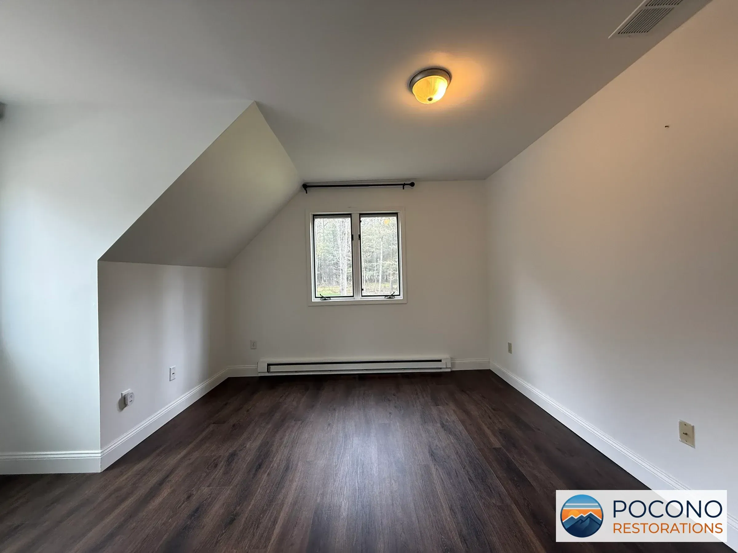 Empty bedroom with a sloped ceiling, dark wood-look flooring, a round ceiling light fixture, a window, and a baseboard heater along the wall.