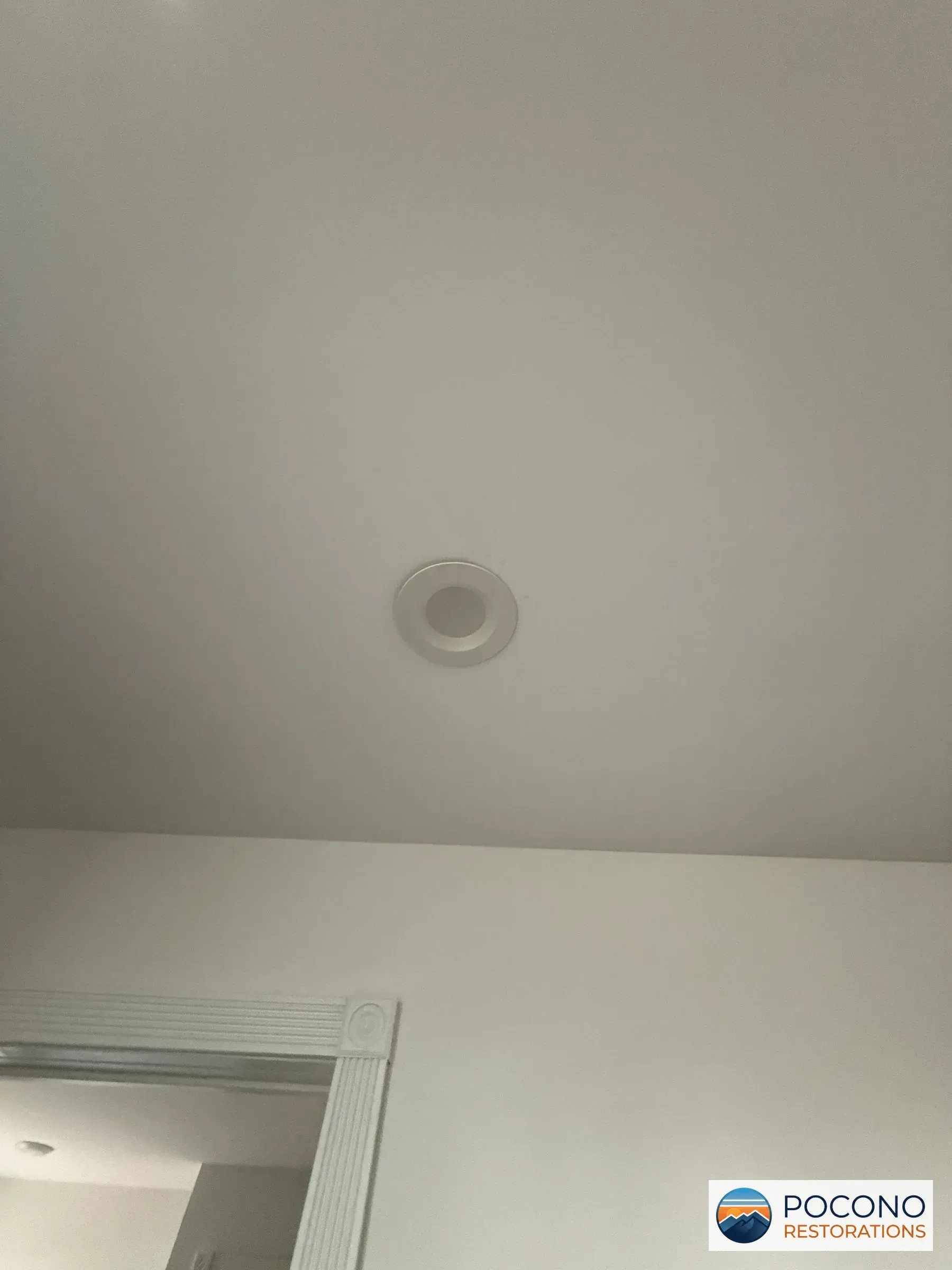Close-up of a ceiling with a round recessed light fixture near a door frame corner.